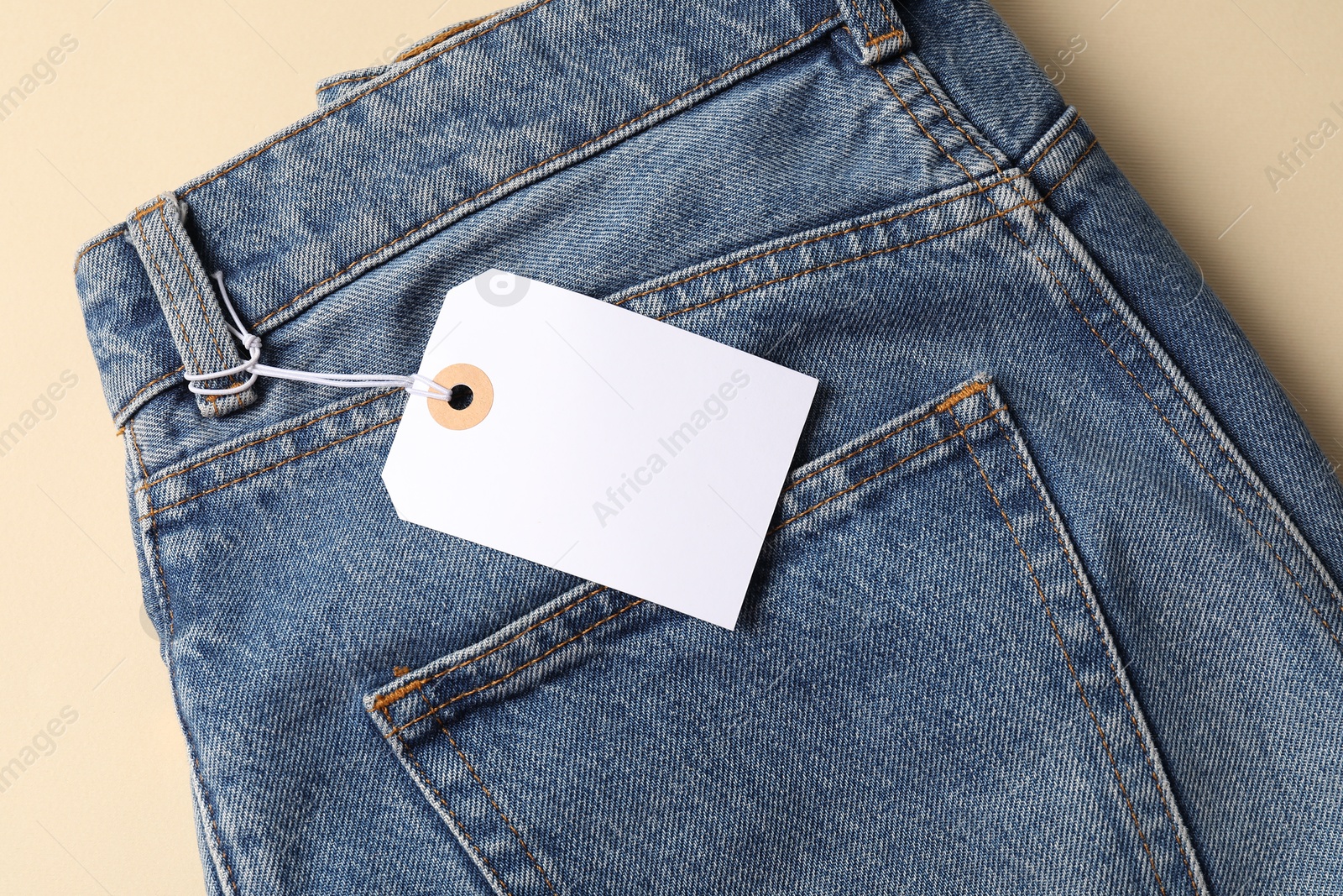 Blue jeans with tag on beige background, top view Photo of Blue jeans with tag on beige background, top view