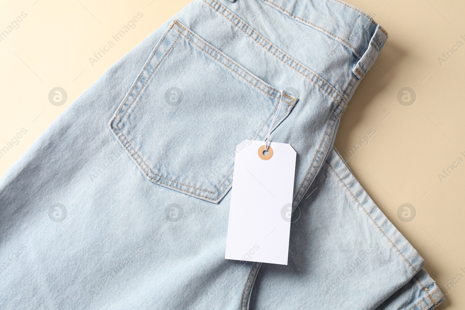 Light blue jeans with tag on beige background, top view Photo of Light blue jeans with tag on beige background, top view