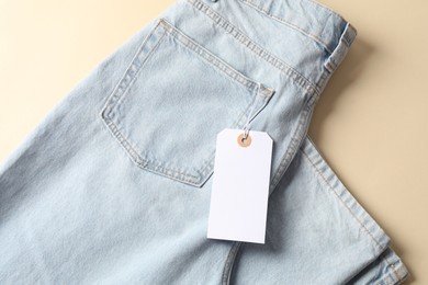 Photo of Light blue jeans with tag on beige background, top view