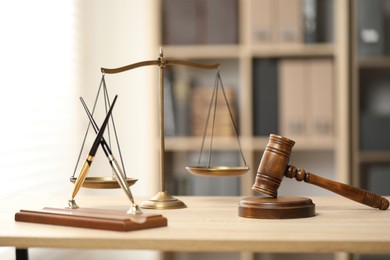 Photo of Judge's gavel, scales and fountain pens on wooden table in office