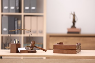 Photo of Judge's gavel, scales, stationery and document tray on wooden table in office