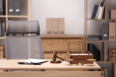 Photo of Judge's gavel, scales, clipboards and document tray on wooden table in office