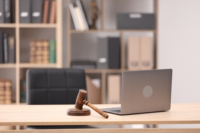 Photo of Judge's gavel and laptop on wooden table in office