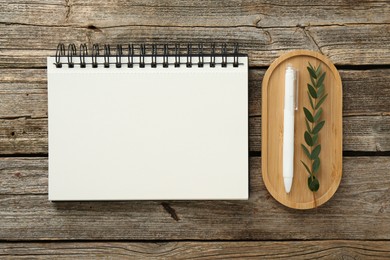 Photo of Notebook, pen and green twig on wooden table, flat lay