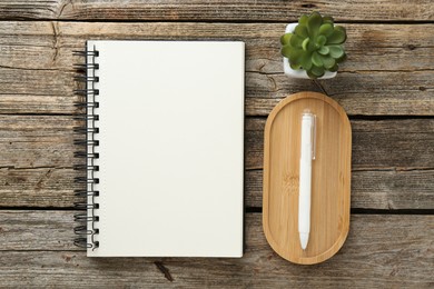 Photo of Notebook, pen and floral decor on wooden table, flat lay