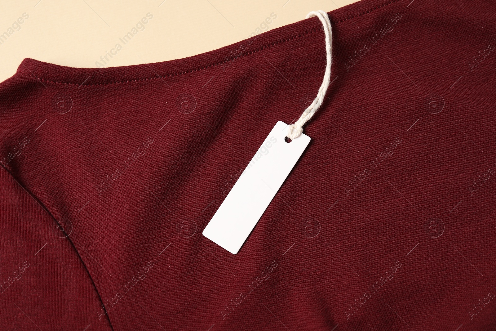 Red garment with tag on beige background, top view Photo of Red garment with tag on beige background, top view