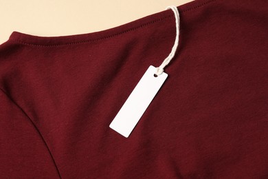 Photo of Red garment with tag on beige background, top view