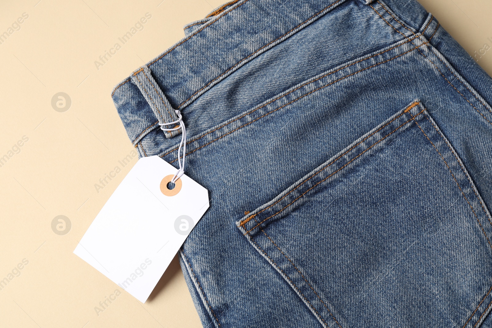 Blue jeans with tag on beige background, top view Photo of Blue jeans with tag on beige background, top view