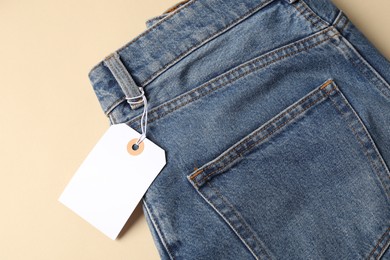 Photo of Blue jeans with tag on beige background, top view
