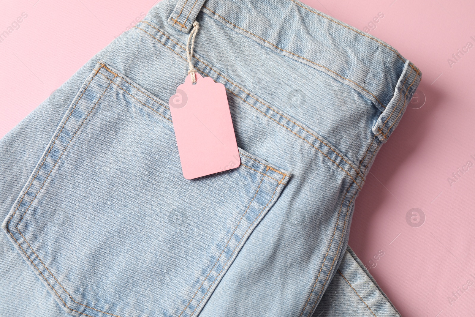 Light blue jeans with tag on pink background, top view Photo of Light blue jeans with tag on pink background, top view