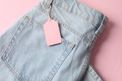 Photo of Light blue jeans with tag on pink background, top view