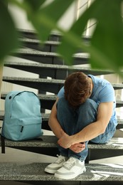 Photo of Teen problems. Depressed teenage boy on stairs indoors