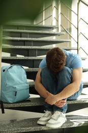 Photo of Teen problems. Depressed teenage boy on stairs indoors