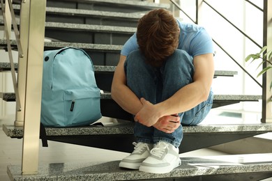Photo of Teen problems. Depressed teenage boy on stairs indoors