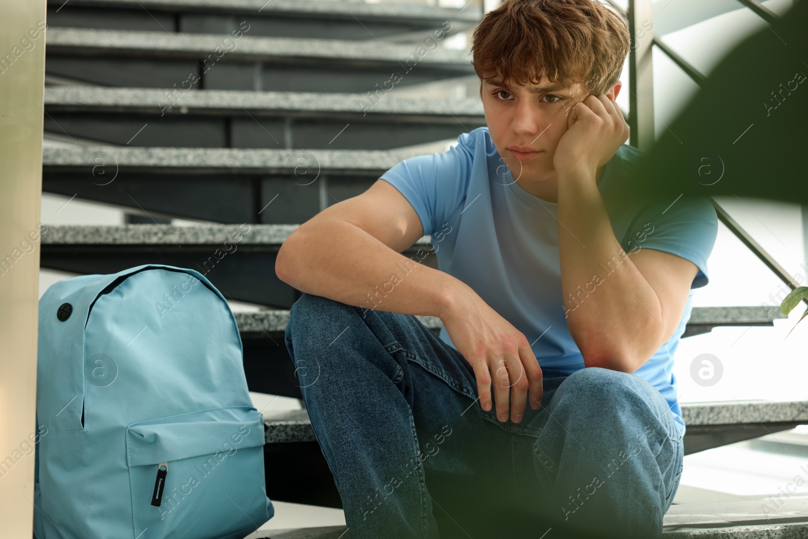 Teen problems. Upset teenage boy on stairs indoors Photo of Teen problems. Upset teenage boy on stairs indoors