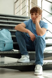 Photo of Teen problems. Upset teenage boy on stairs indoors