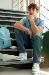 Photo of Teen problems. Upset teenage boy on stairs indoors