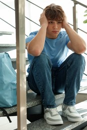 Photo of Teen problems. Upset teenage boy on stairs indoors