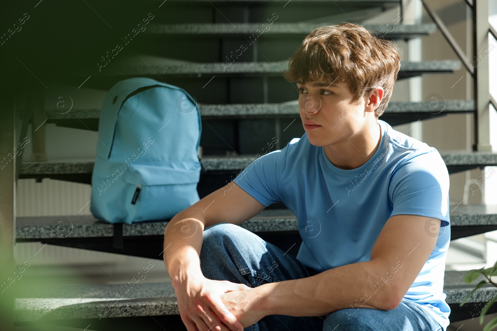 Teen problems. Upset teenage boy on stairs indoors Photo of Teen problems. Upset teenage boy on stairs indoors