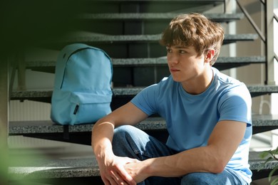 Photo of Teen problems. Upset teenage boy on stairs indoors
