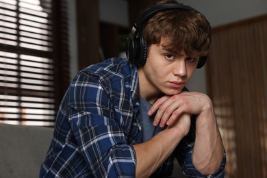 Photo of Teen problems. Upset teenage boy in headphones at home