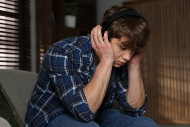 Photo of Teen problems. Upset teenage boy in headphones at home