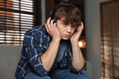 Photo of Teen problems. Upset teenage boy in headphones at home