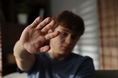 Photo of Teen problems. Upset teenage boy making stop gesture at home, selective focus