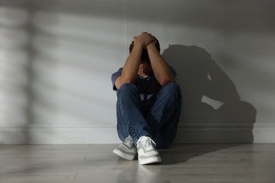 Photo of Teen problems. Upset teenage boy near light wall indoors
