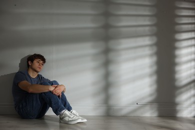 Photo of Teen problems. Upset teenage boy near light wall indoors, space for text