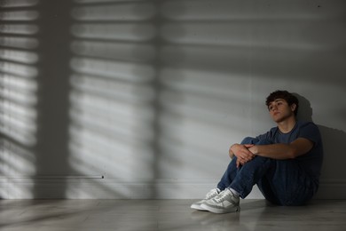 Photo of Teen problems. Upset teenage boy near light wall indoors, space for text