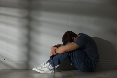 Photo of Teen problems. Upset teenage boy near light wall indoors, space for text