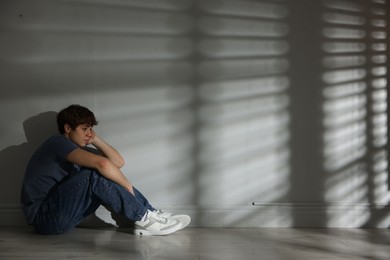 Photo of Teen problems. Upset teenage boy near light wall indoors, space for text