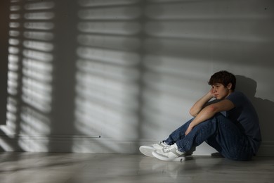 Photo of Teen problems. Upset teenage boy near light wall indoors, space for text