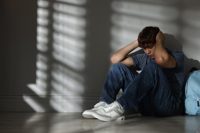 Photo of Teen problems. Upset teenage boy with backpack near light wall indoors, space for text
