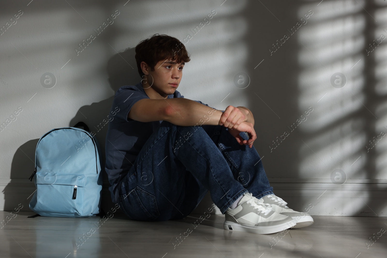 Teen problems. Upset teenage boy with backpack near light wall indoors Photo of Teen problems. Upset teenage boy with backpack near light wall indoors
