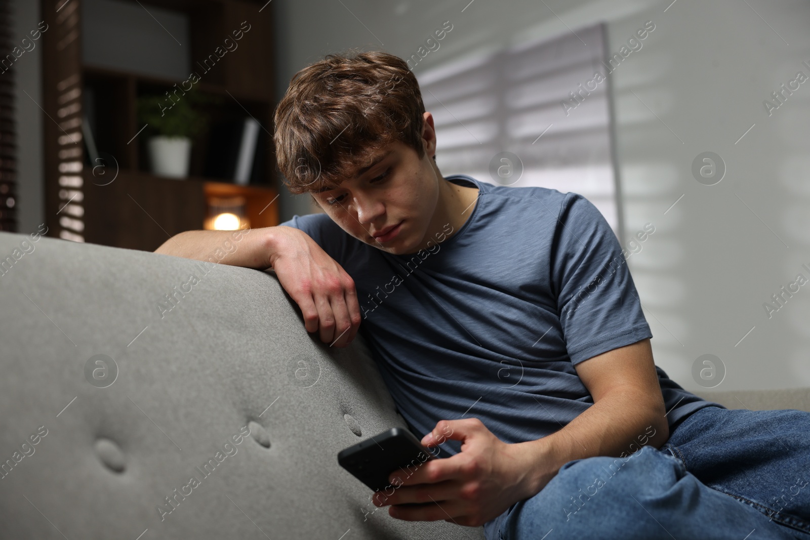 Teen problems. Upset teenage boy in smartphone on sofa at home Photo of Teen problems. Upset teenage boy in smartphone on sofa at home