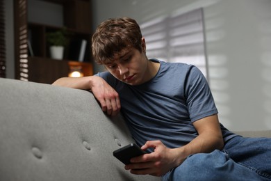 Photo of Teen problems. Upset teenage boy in smartphone on sofa at home