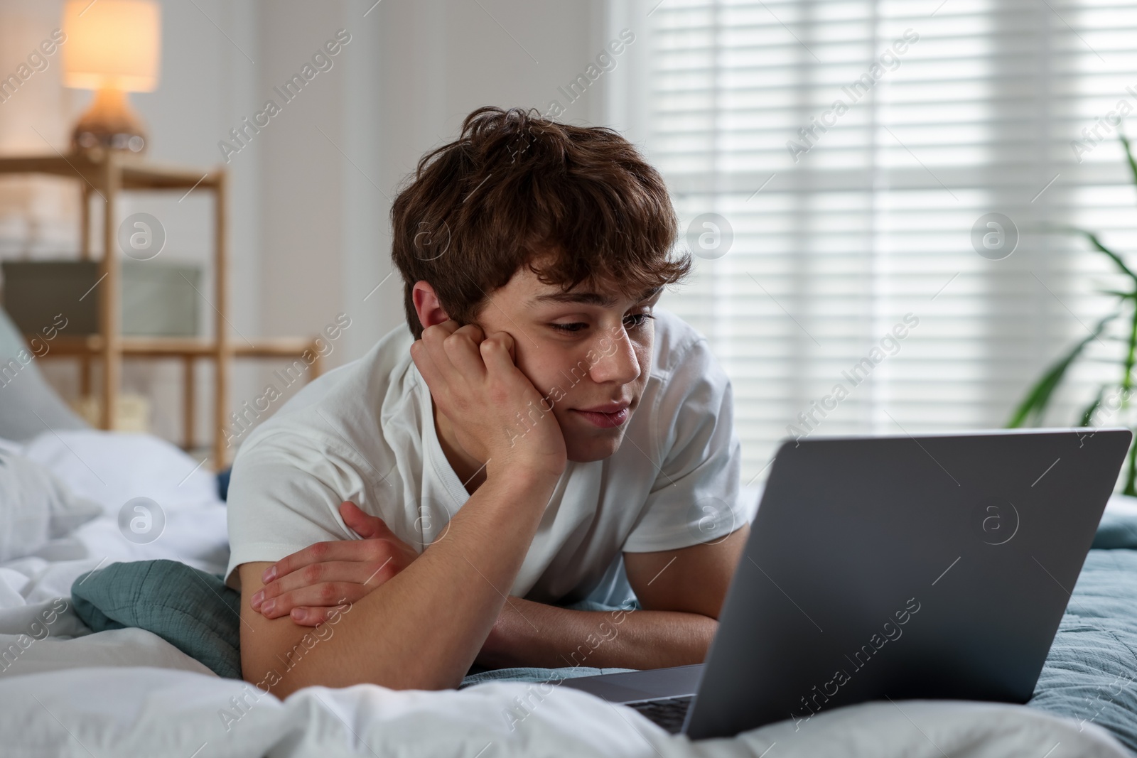 Teen problems. Upset teenage boy with laptop on bed at home Photo of Teen problems. Upset teenage boy with laptop on bed at home