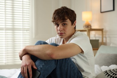 Photo of Teen problems. Upset teenage boy with smartphone on bed at home