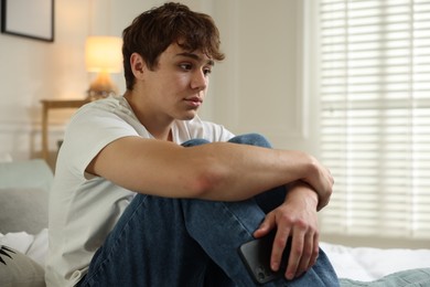 Photo of Teen problems. Upset teenage boy with smartphone on bed at home