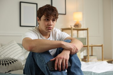 Photo of Teen problems. Upset teenage boy with smartphone on bed at home