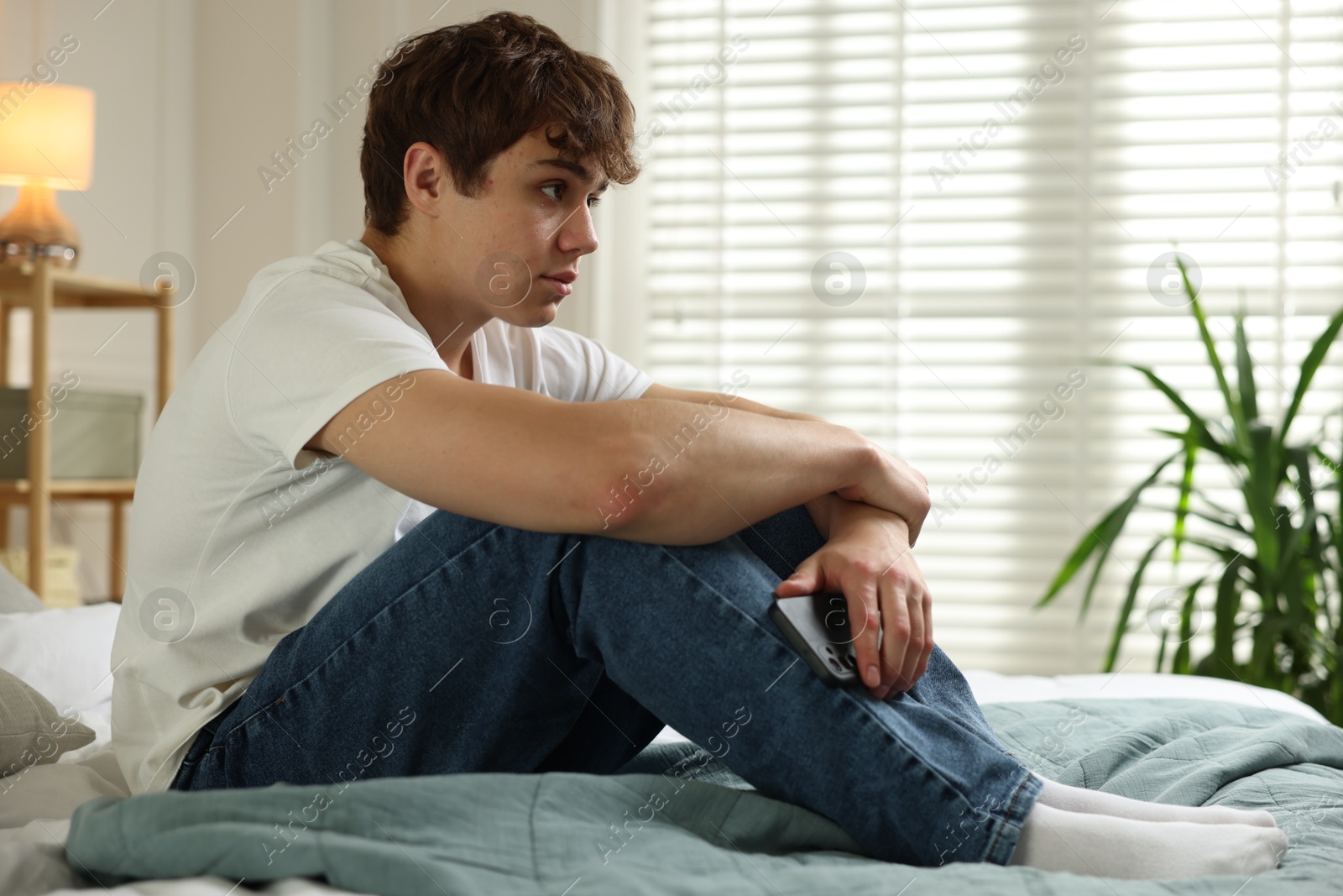 Photo of Teen problems. Upset teenage boy with smartphone on bed at home