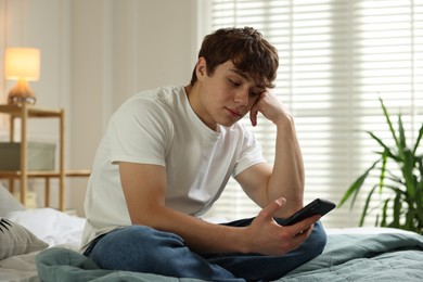 Photo of Teen problems. Upset teenage boy with smartphone on bed at home
