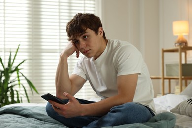 Photo of Teen problems. Upset teenage boy with smartphone on bed at home