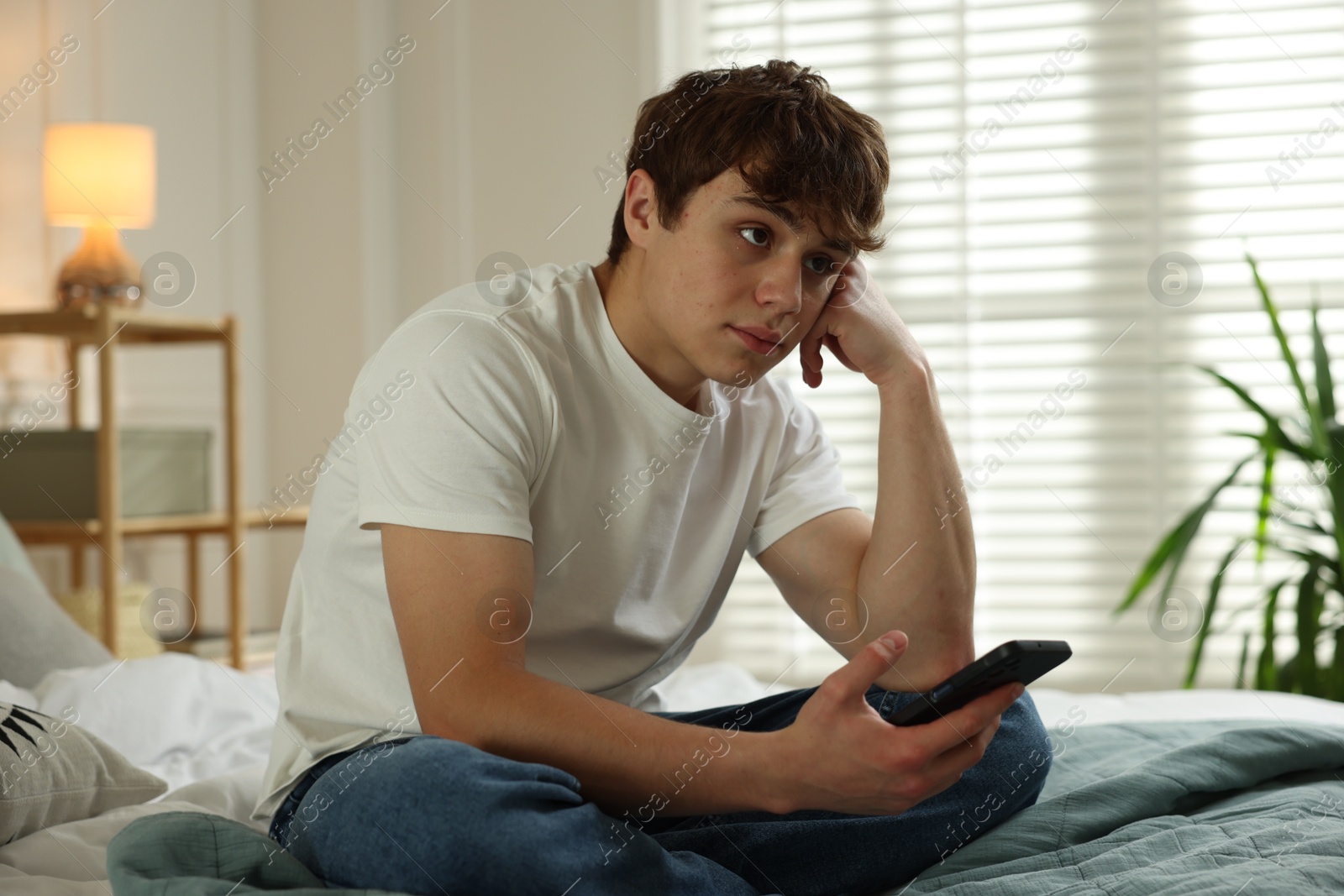 Teen problems. Upset teenage boy with smartphone on bed at home Photo of Teen problems. Upset teenage boy with smartphone on bed at home