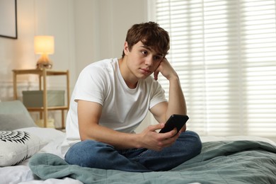 Photo of Teen problems. Upset teenage boy with smartphone on bed at home