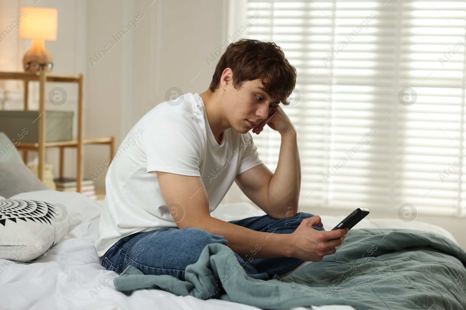 Teen problems. Upset teenage boy with smartphone on bed at home Photo of Teen problems. Upset teenage boy with smartphone on bed at home