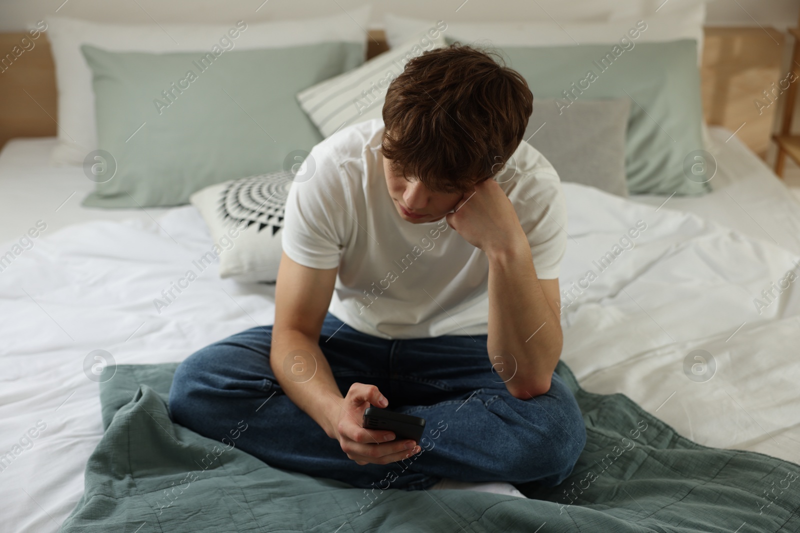 Teen problems. Upset teenage boy with smartphone on bed at home Photo of Teen problems. Upset teenage boy with smartphone on bed at home
