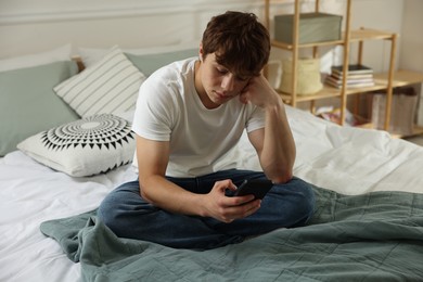 Photo of Teen problems. Upset teenage boy with smartphone on bed at home